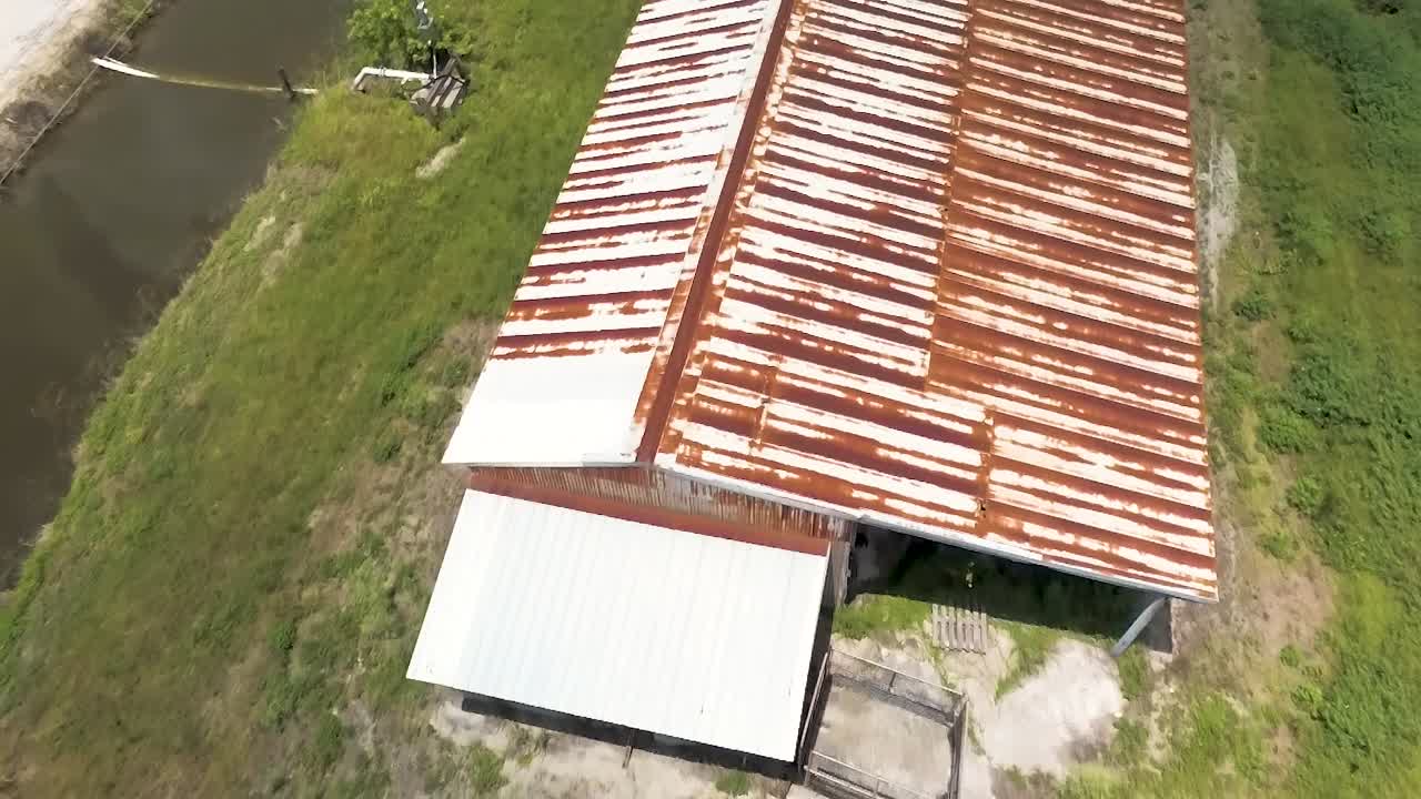toma aérea de una estructura antigua con techo de metal oxidado en tierras agrícolas