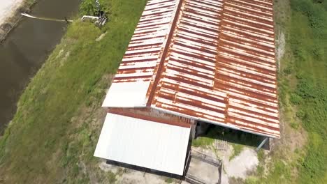 Aerial-shot-of-old-structure-with-rusted-metal-roof-on-farm-land