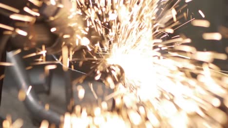 bright sparks flying from grinder grinding metal pipe in a factory - close up