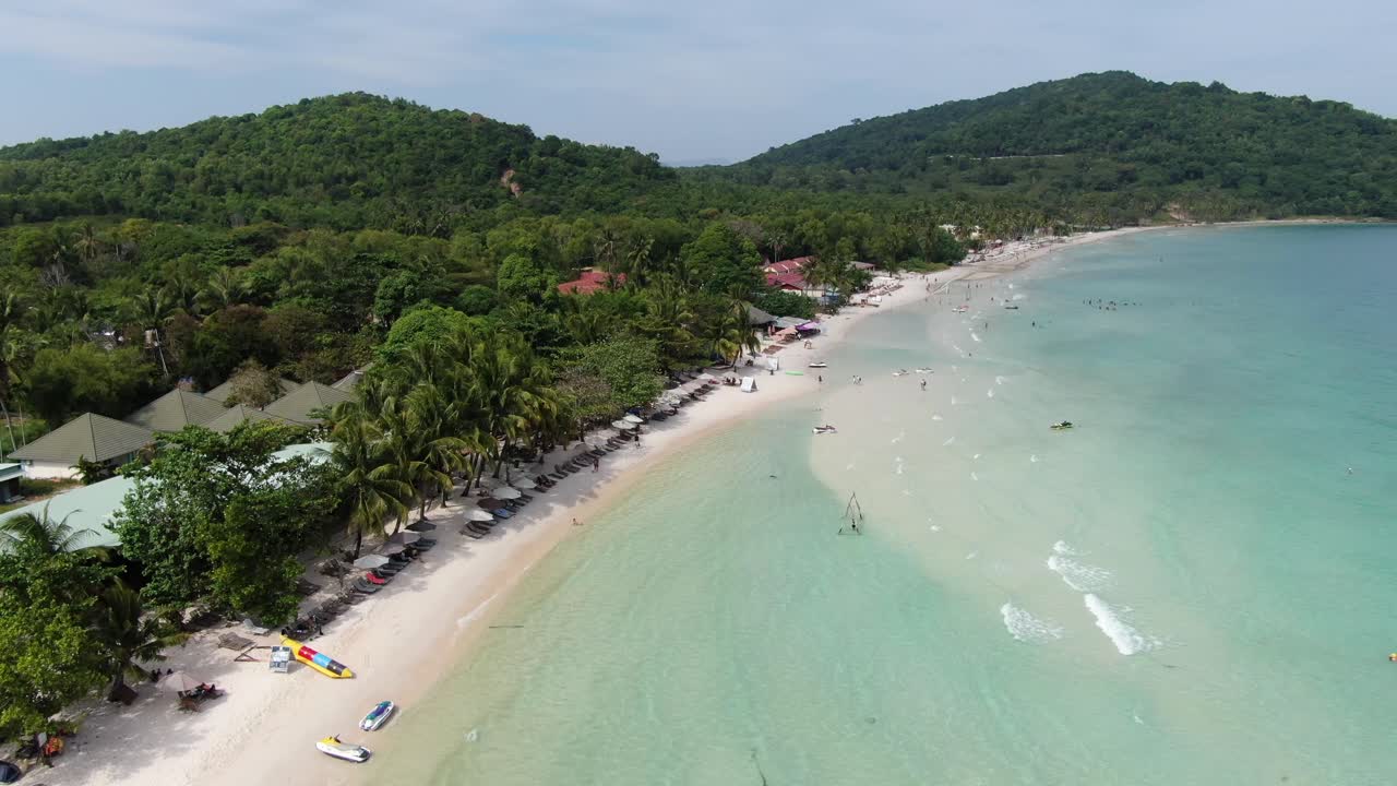 Drone aerial view in Vietnam flying over Phu Quoc island Sao beach, white sand, crystal clear blue turquoise water, green palm trees forest and people walking on a sunny day