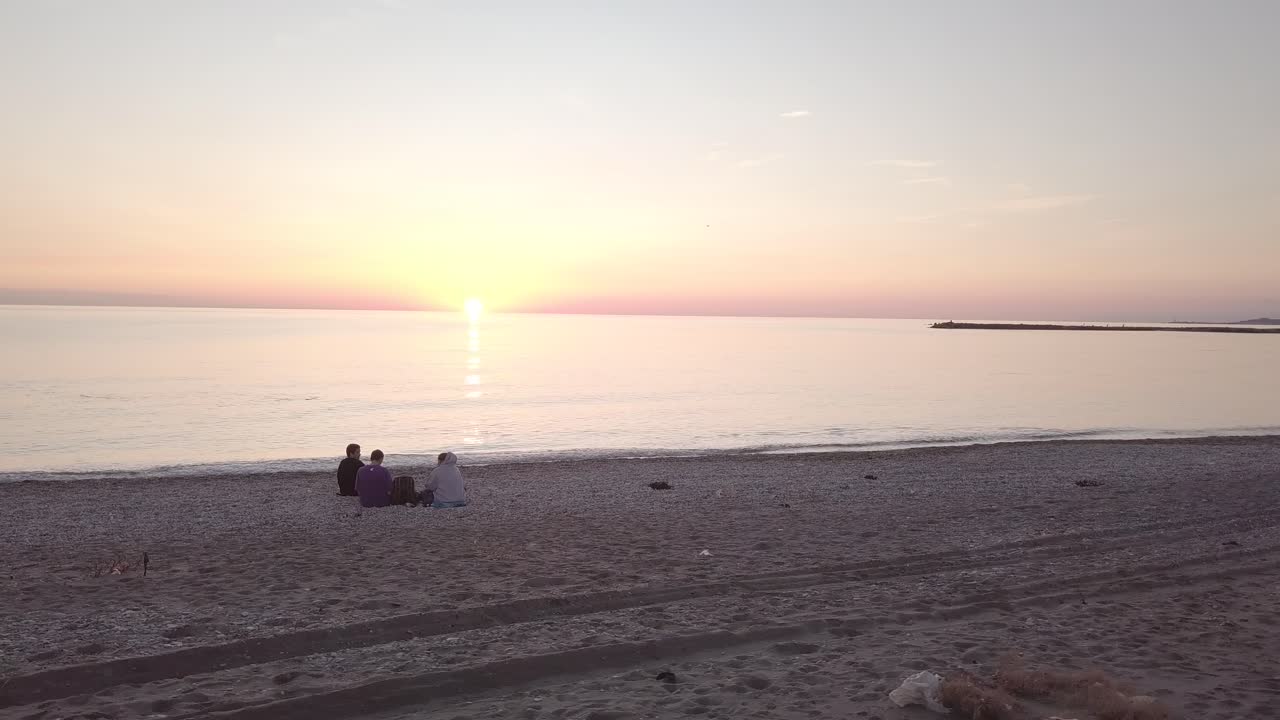 three friends sitting on the beach watching the sunset