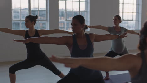 yoga class of healthy pregnant women practicing warrior pose enjoying group physical fitness workout with instructor in studio at sunrise