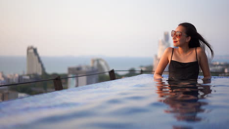 glamorous asian woman sitting in a rooftop infinity pool overlooking city