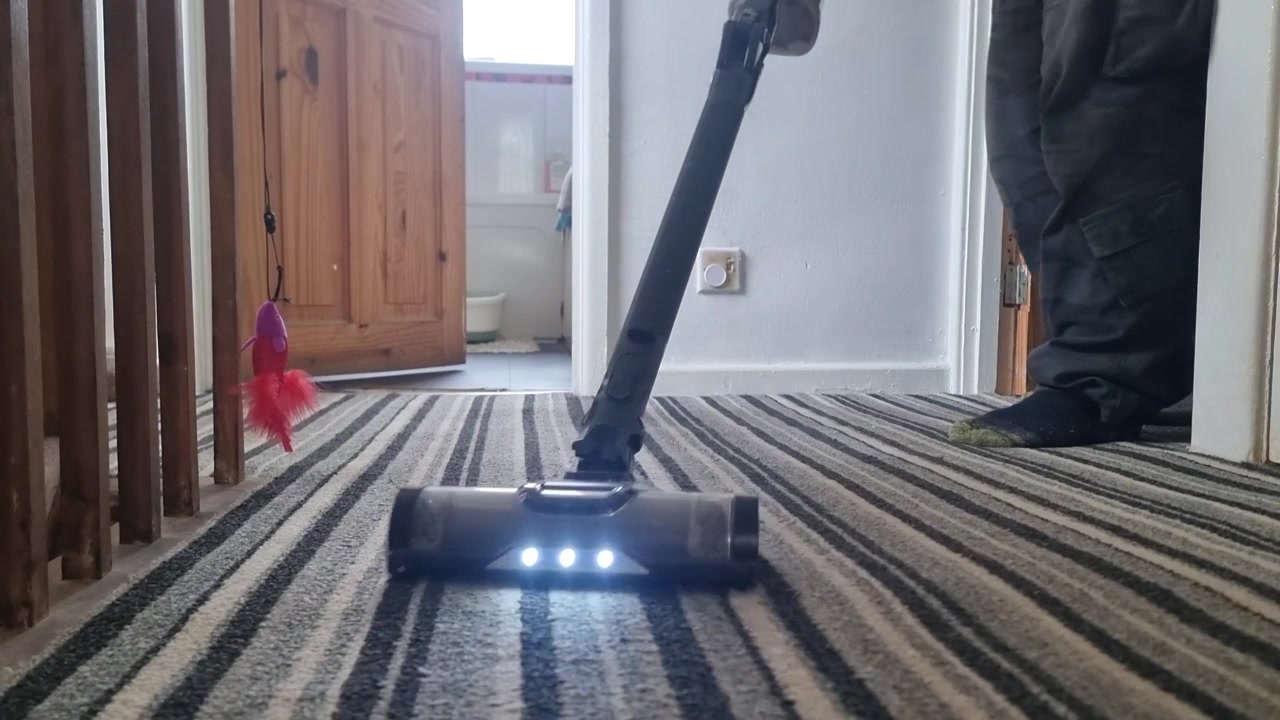 Low angle male wearing socks cleaning striped landing carpet with upright modern hoover device