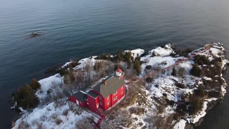 red lighthouse located in marquette, michigan in winter with rotating drone shot