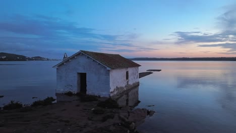 Fornells-Bay-Bootshaus-Mit-Drohne,-Die-Zur-Blauen-Stunde-Fliegt