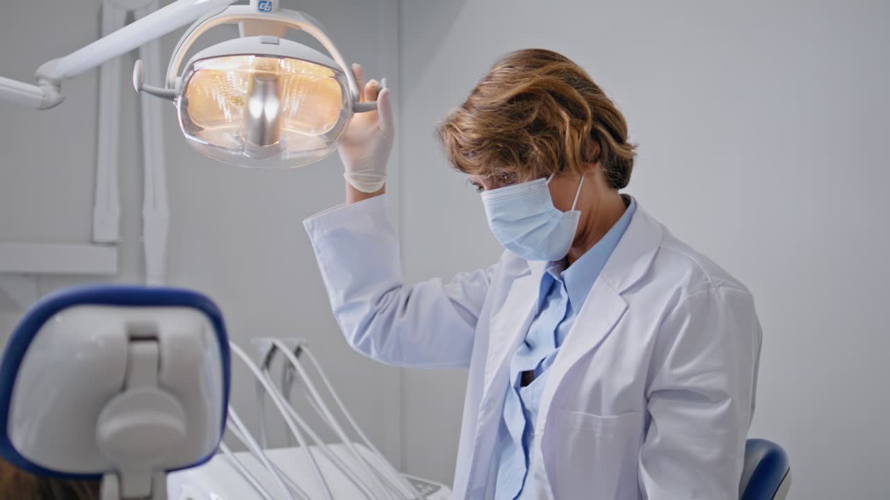 Woman dentist adjusting lamp to dental examination young patient closeup