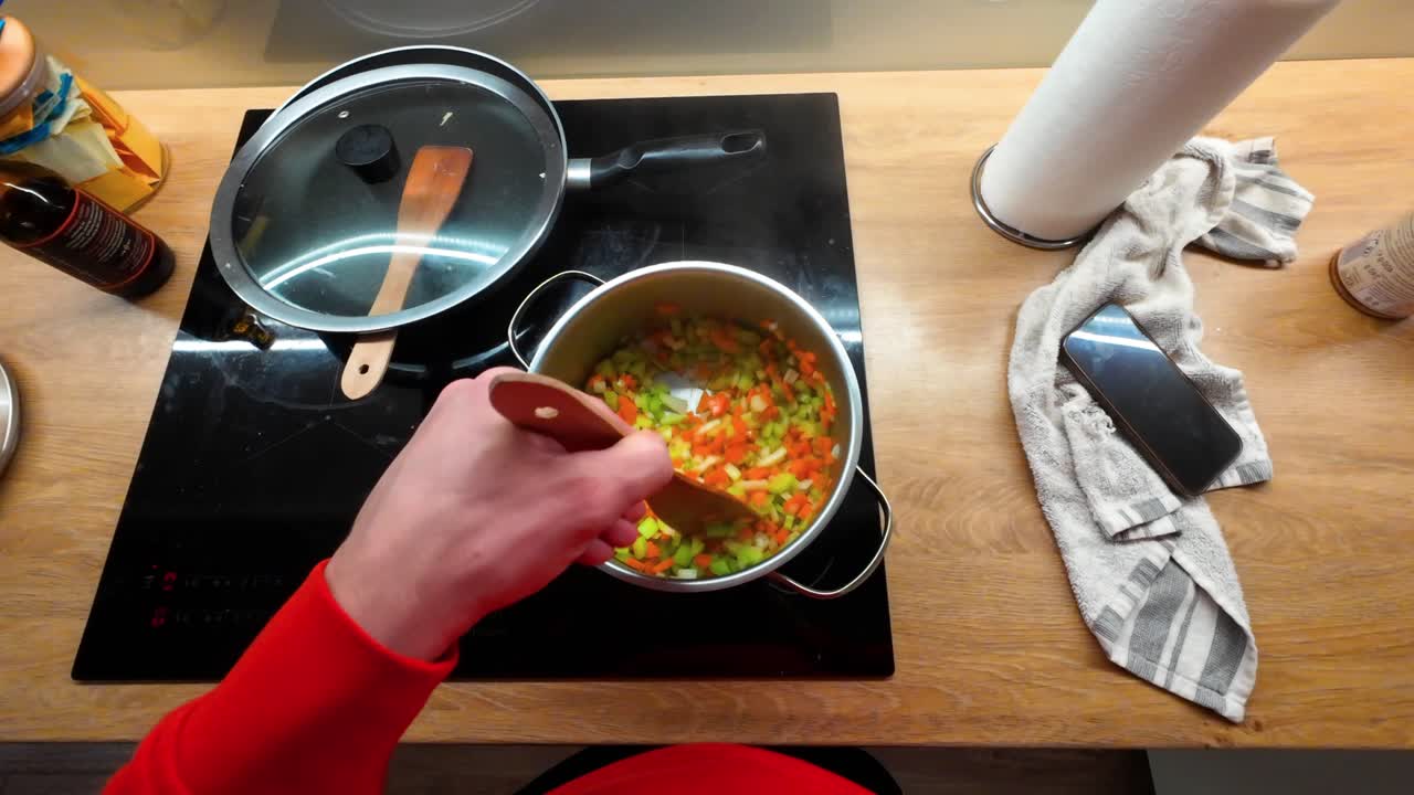 Zbliżenie kolorowych warzyw mieszanych w garnku na nowoczesnej płycie kuchennej. Ciepłe wnętrze kuchni z żywymi składnikami i naturalnym oświetleniem, idealne do scen kulinarnych.