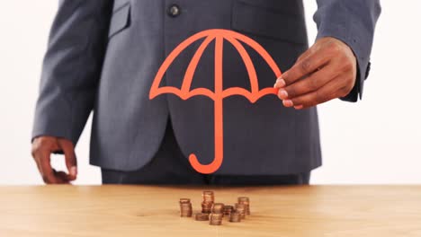 mid section of businessman holding paper cutout of umbrella on stacks of coins