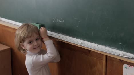 girl drawing at blackboard using a chalk in classroom. education process