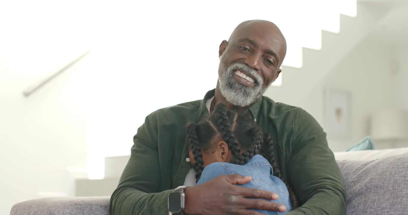 Mature African man and child, child approaching while man placing arm and comforting on sofa
