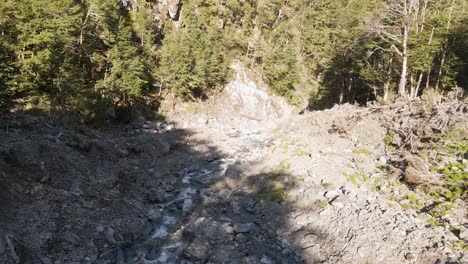 Drone-flight-down-a-river-bed-after-a-rainstorm-within-dense-forest-in-warm-sunlight