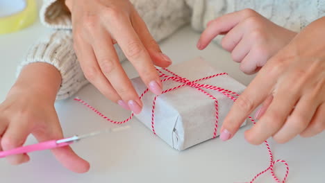 child decorates the bow of a wrapped christmas gift with a paper tree