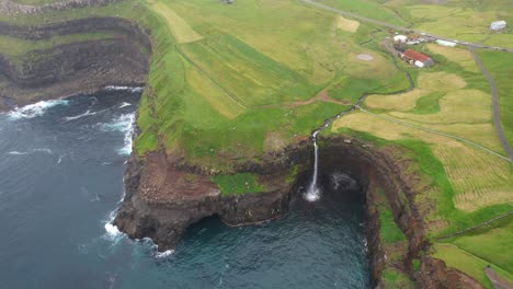 toma aérea de arriba hacia abajo de la caída de la cascada de mulafossur en el océano atlántico y el paisaje verde en la parte superior