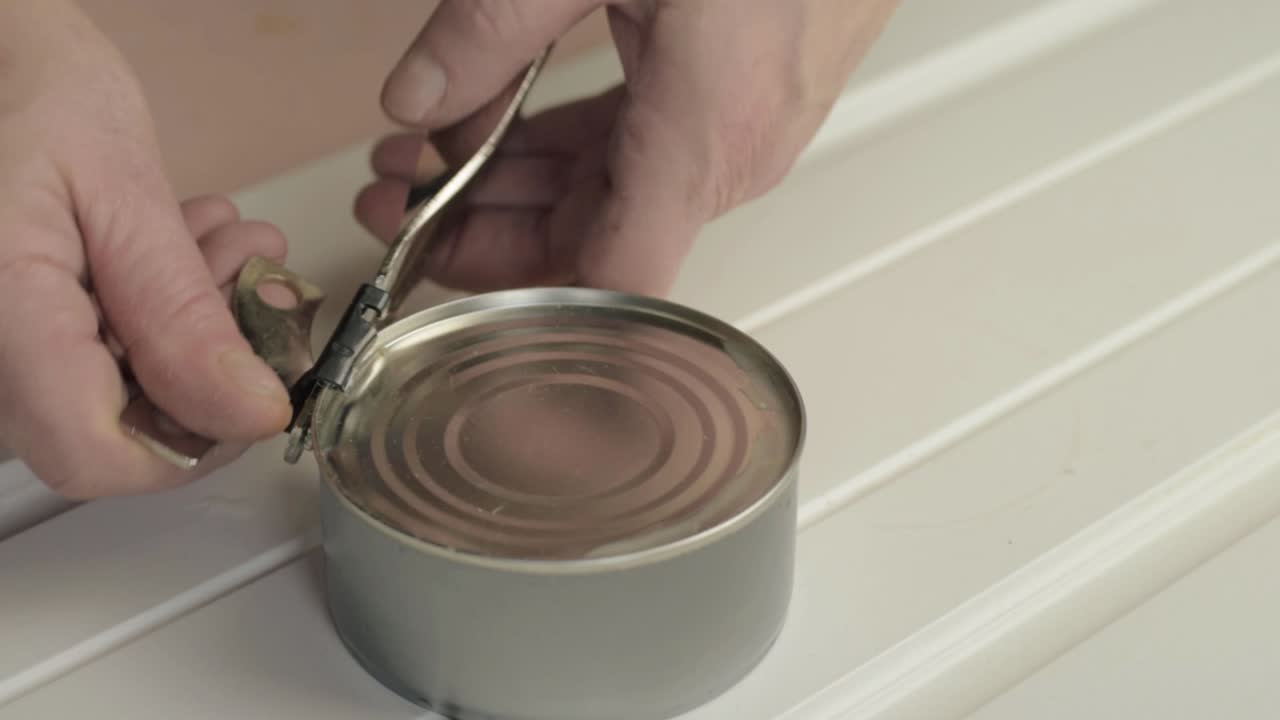 Hands opening can of tuna with tin opener close up shot