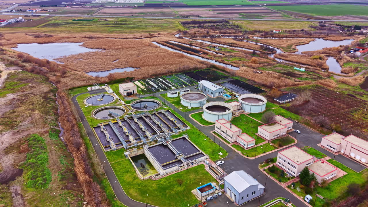 Water treatment facility located in a rural area with large tanks and buildings surrounded by greenery and water bodies during daylight hours