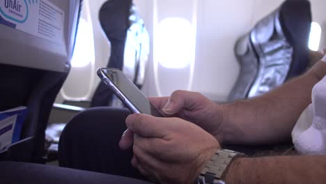 hombre de negocios que viaja en avión usando un teléfono móvil durante el vuelo, desplazándose y escribiendo y haciendo gestos con las manos