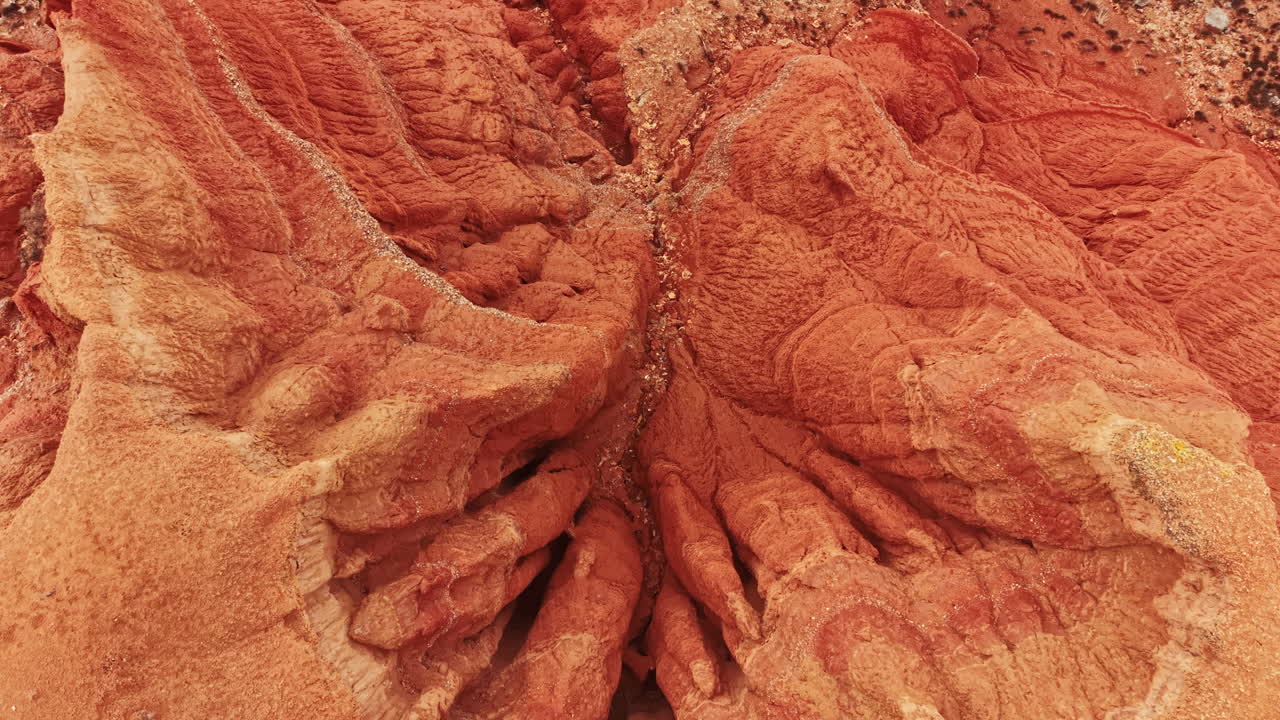 Paesaggio di canyon che mostra formazioni rocciose rosse con texture e motivi unici sotto la luce intensa del sole a mezzogiorno.