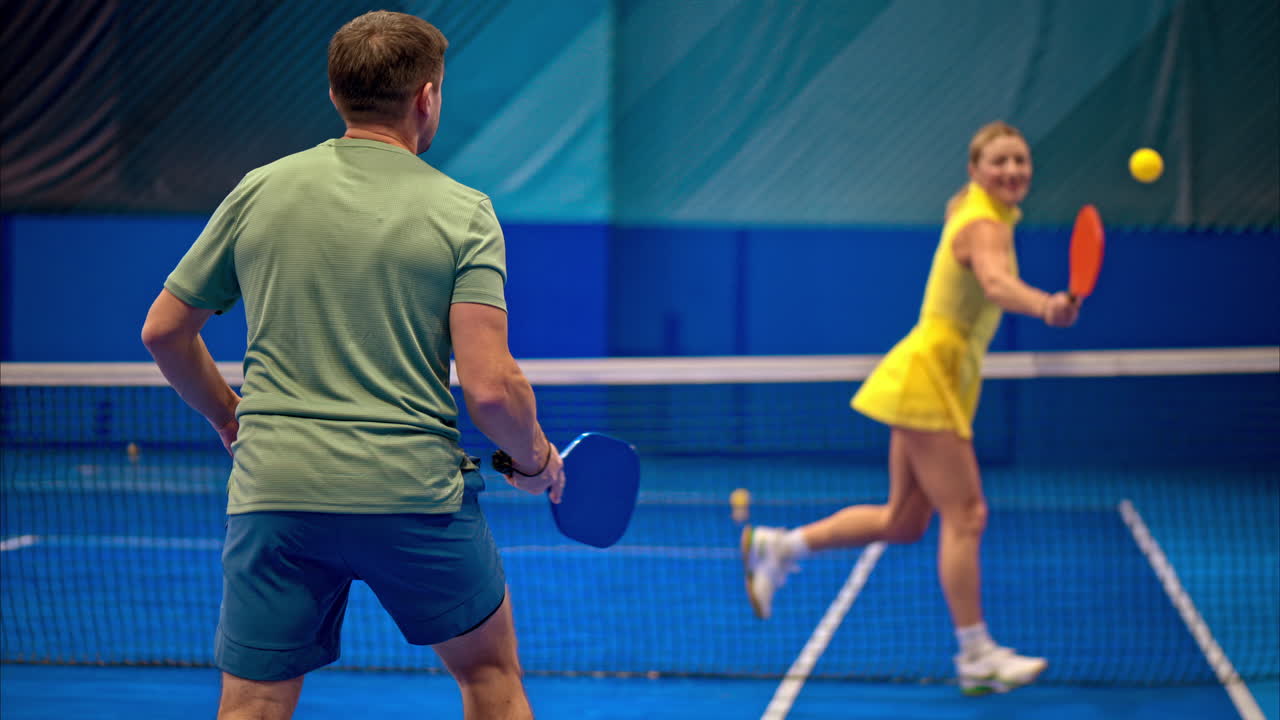 Slow motion of man and a woman training to play pickleball on a blue, inside court