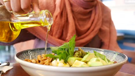 woman pouring olive oil on a salad with avocado and walnuts