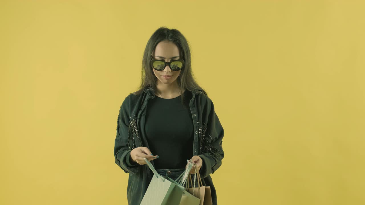 joven hermosa mirando en la bolsa de compras en el fondo amarillo