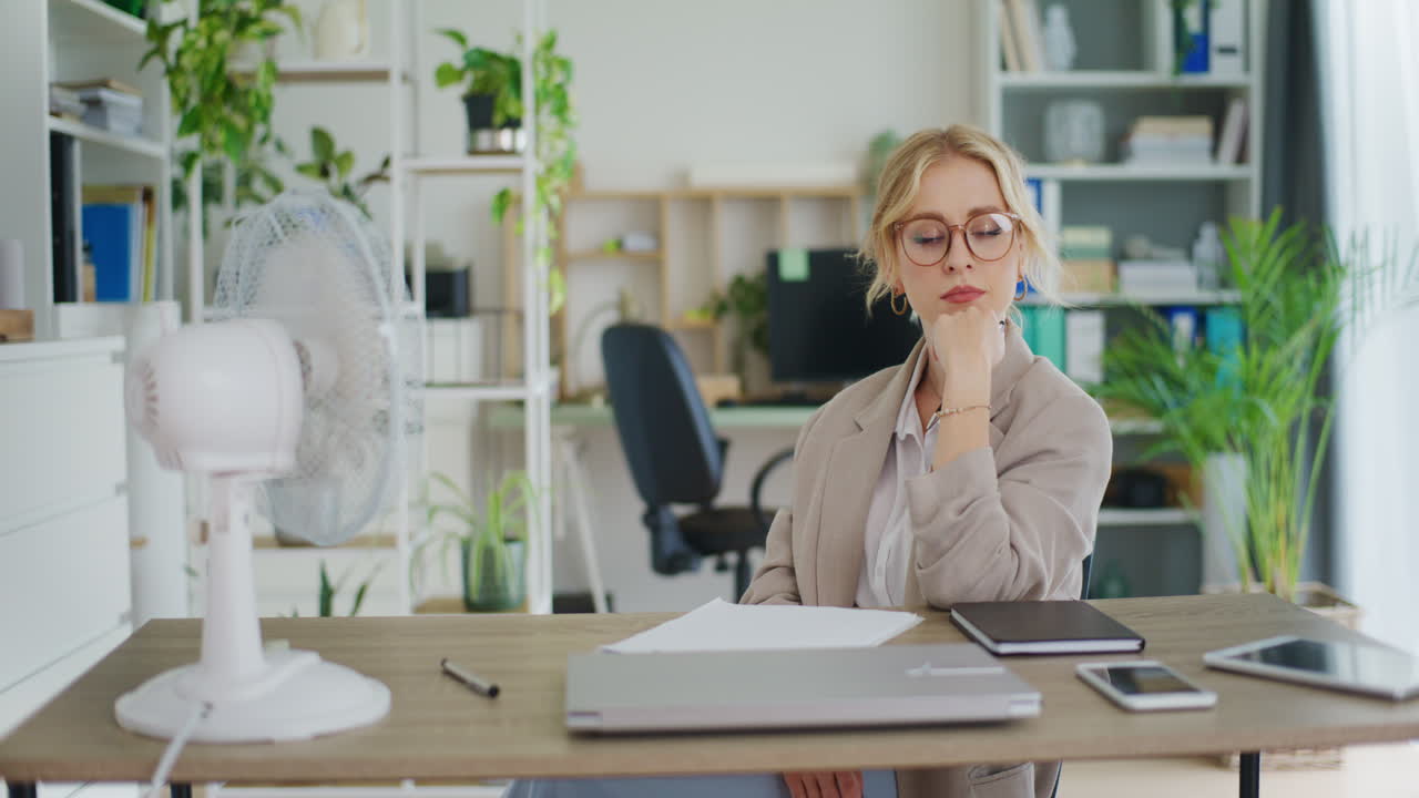 una mujer de negocios se enfría con un ventilador en la oficina.