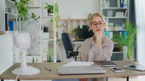 businesswoman cools down with fan in office