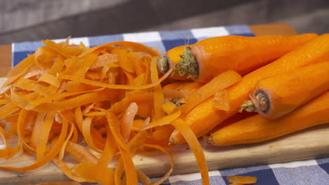 pile of fresh, whole, raw, carrots and peels on a cutting board