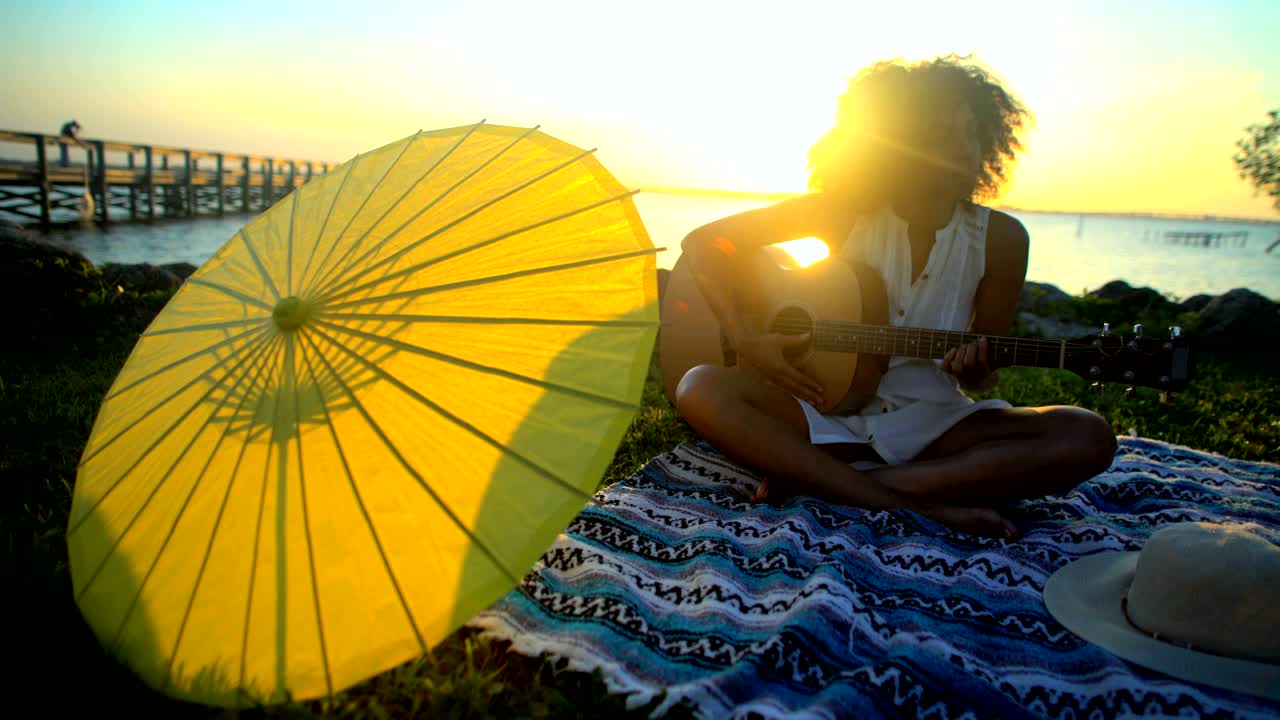 mujer afroamericana disfrutando de un picnic en la playa tocando la guitarra