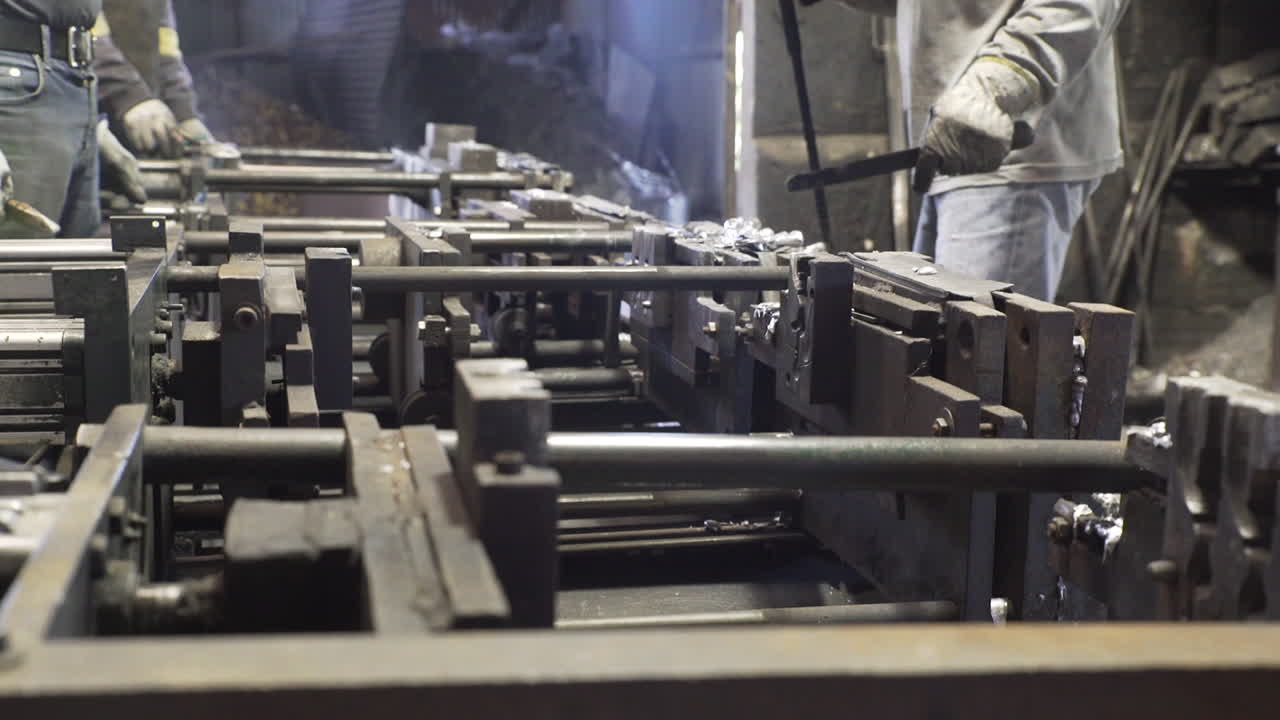 Sidovy av personer som tar bort metallföremål från formar i en fabrik.