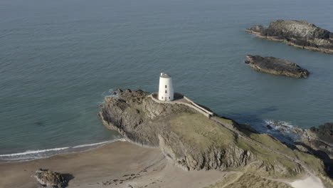 an aerial view of twr mawr lighthouse on ynys llanddwyn island, flying right to left around the lighthouse while zooming in, anglesey, north wales, uk