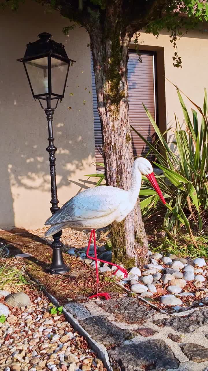 Vertical view of a decorative "false" stork French garden statue near house wall with lantern and plants in small front courtyard