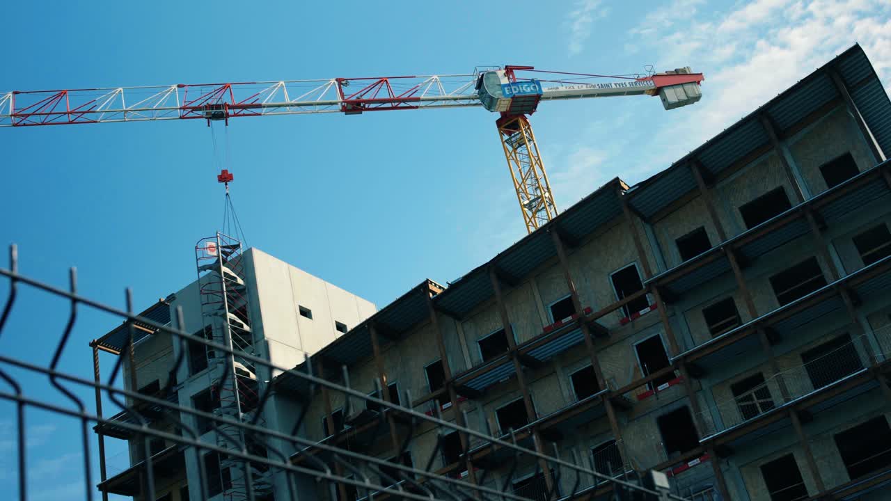 Low angle view of a tall construction crane towering over an unfinished concrete building frame. Industrial development scene capturing urban growth and structural engineering in progress