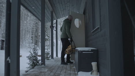 man carries chopped timber through porch and into cabin