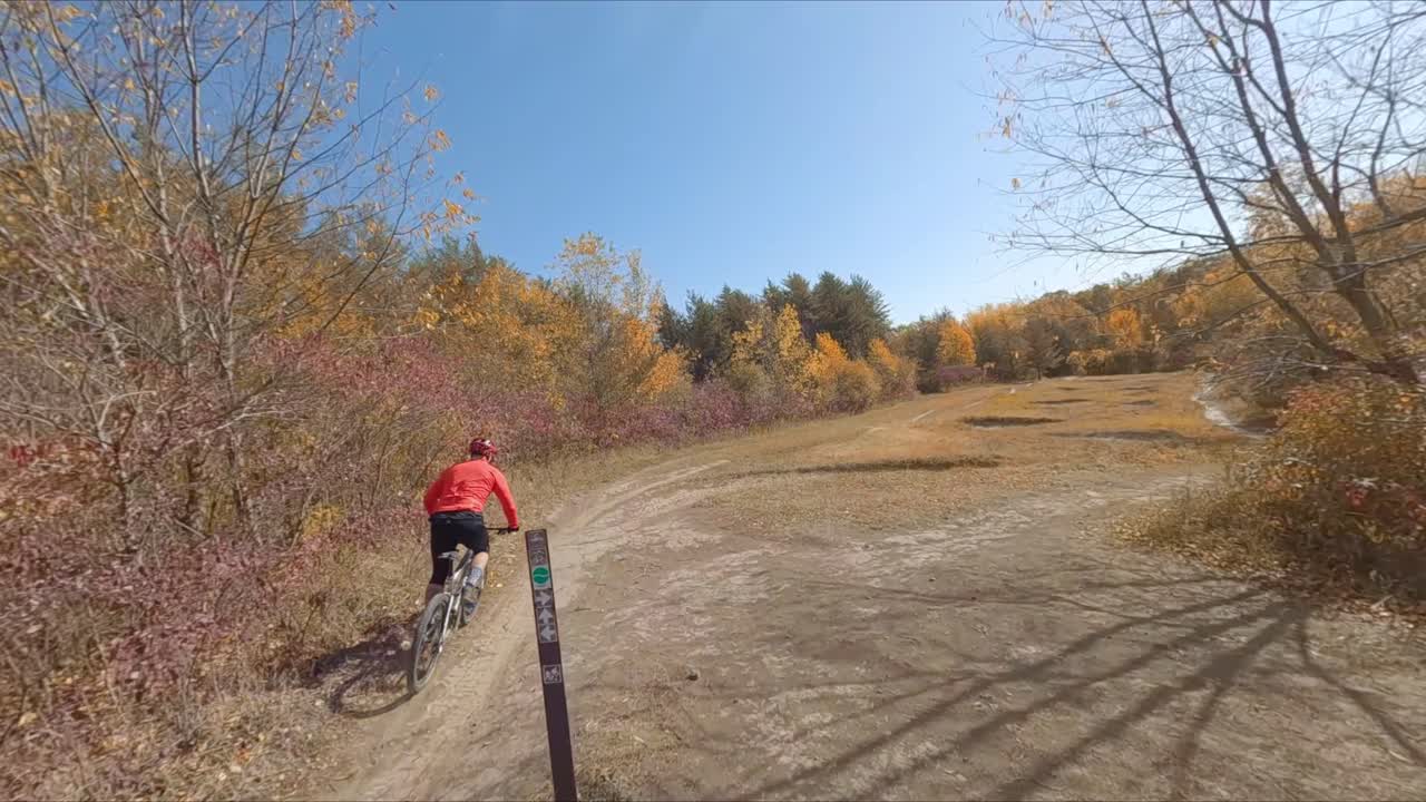 fpv drone siguiendo a un ciclista de montaña masculino en bicicleta por un sendero de tierra durante el día de otoño