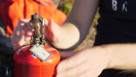 primer plano de perfil de la persona que abre el soporte de la bandeja de metal en un calentador de combustible de camping de propano naranja, al aire libre en un entorno de camping