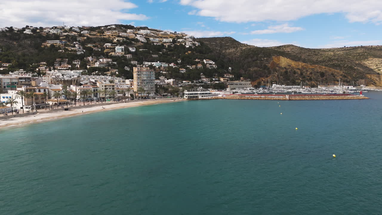 Turquoise waters meet gentle shore along stone barrier in Xabia, Spain