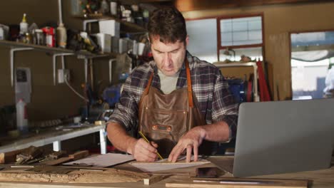 focused caucasian male knife maker in workshop making drawing