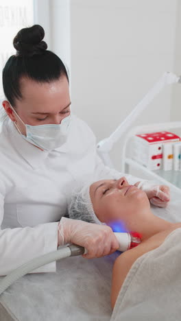 beautician makes woman rf lifting cosmetology procedure of face and eyes area collagen mask at spa