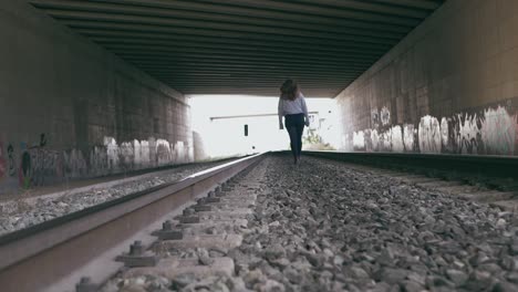 young woman walks between the train tracks in a tunnel full of graffiti