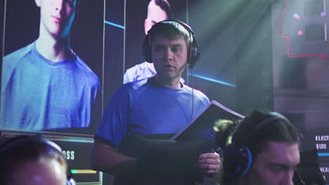 male coach checking gamers during tournament gamer in headset reading game strategy and speaking to team of cyber sportsmen during professional esports competition
