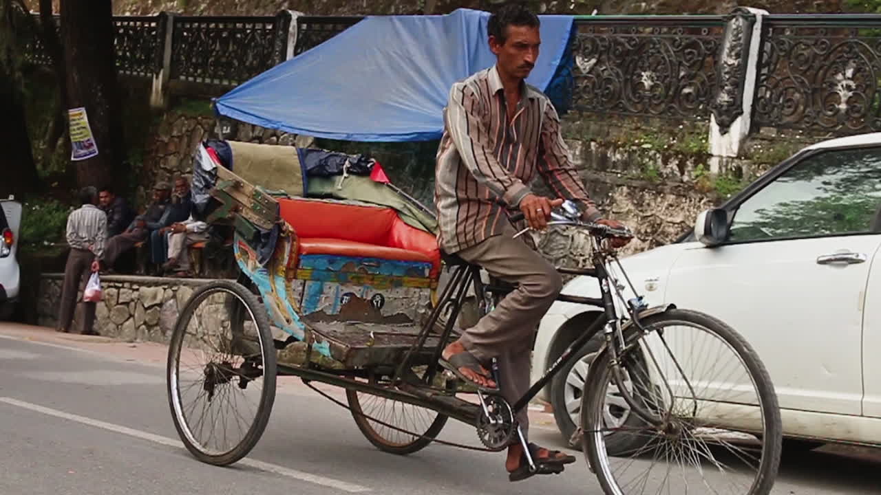 Tourists and a cycle rickshaw tuk tuk rider passes by on Mall Road, Mussoorie, Uttarakhand, India, slow motion shot.