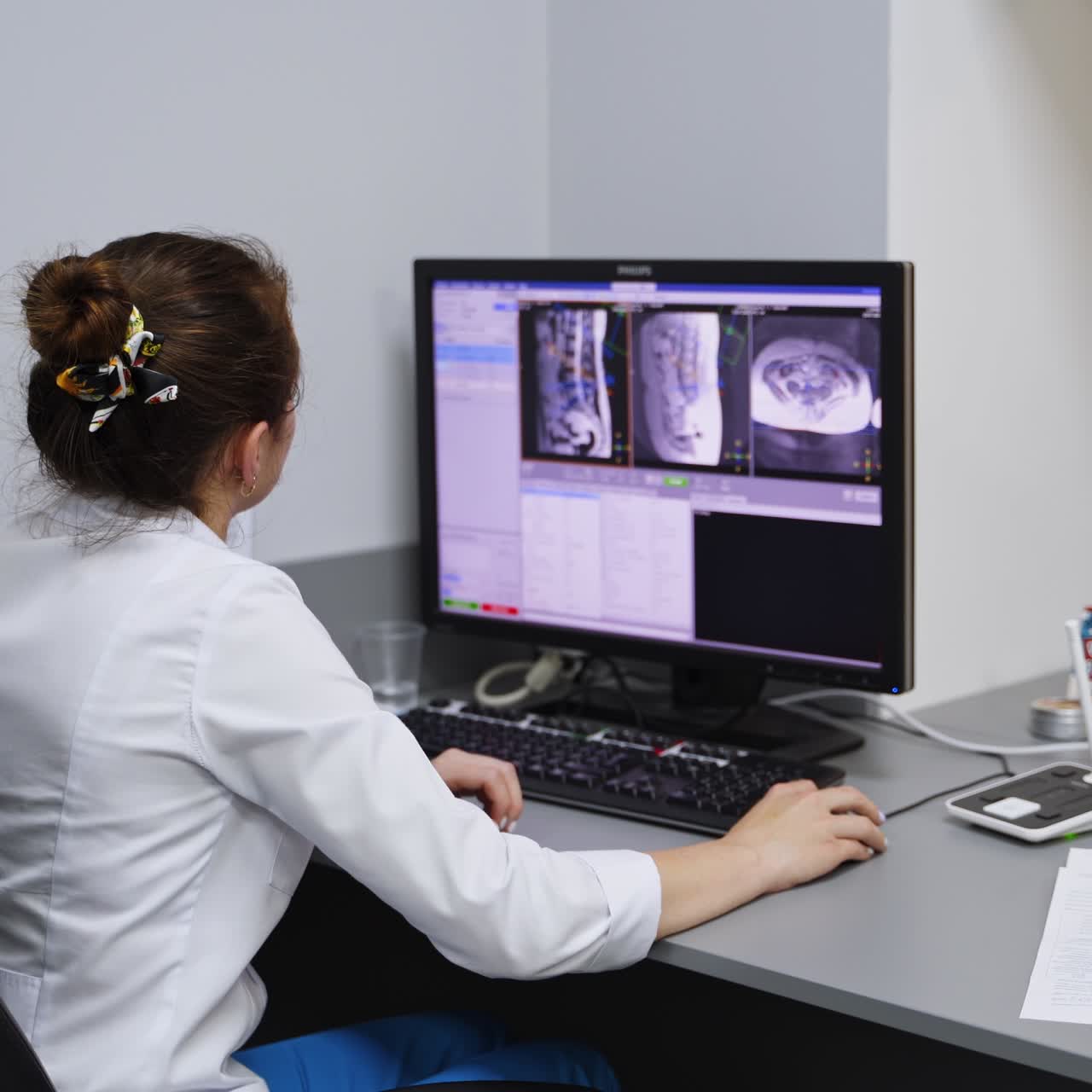 Technician working in a hospital lab sitting in front of computer. Medic analyses the MRI scans of a patient. Rear view