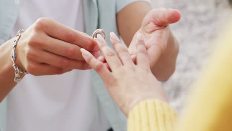 Mid-section-of-african-american-man-putting-a-ring-on-his-girlfriend's-finger-on-rocks-near-the-sea