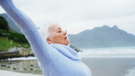 senior woman standing with hands raised on beach