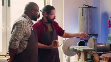 manufacturer teaching new employee how to shape wooden bowl on disc sander