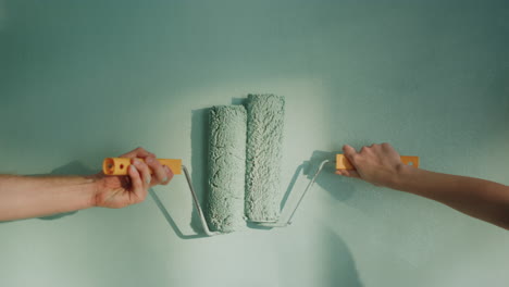 unknown woman leading roller on wall. man hand holding paint roller on surface.