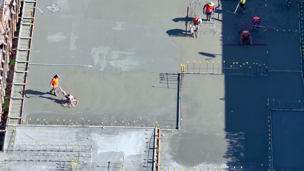 Aerial view of workers using power trowels to finish concrete slab in bright daylight