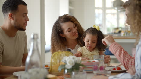 couple, young girl and adult friends talk at kitchen table