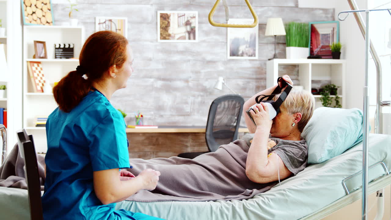 Female nurse in retirment home giving an old disabled lady a VR headset
